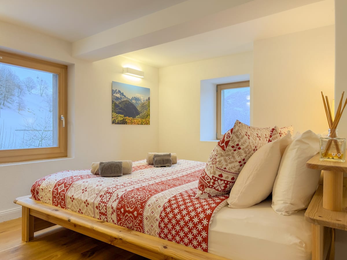 The queen bedroom at Casa Peuti, red-and-white bedding and a snowy Petit Combin view through the window